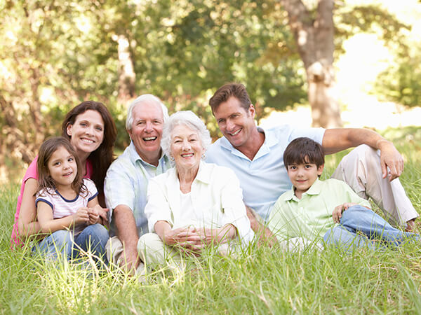 A family of parents and two grandparents sitting on the grass in a park while smiling and hugging
