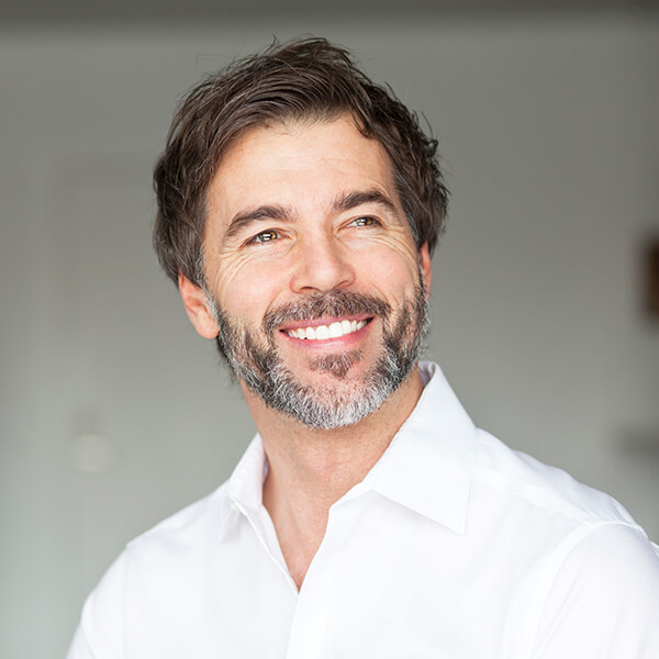 A mature man with white shirt, beard, and black hair ready for his restorative dentistry treatment