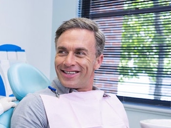 Mature man sitting in a dental chair looking to the right as he waits enjoy our services