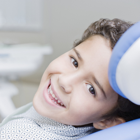 Young boy laying a in dental chair and looking back while smiling